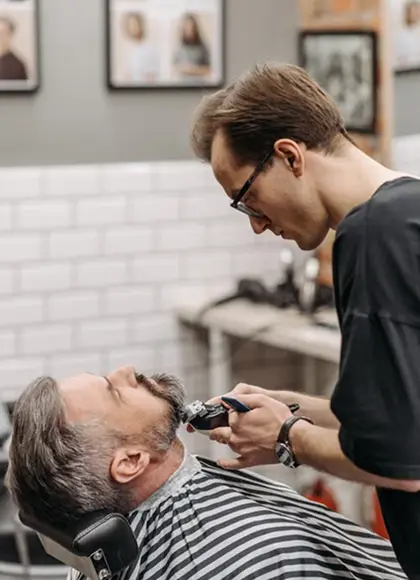 Barber trimming an older client's beard with clippers