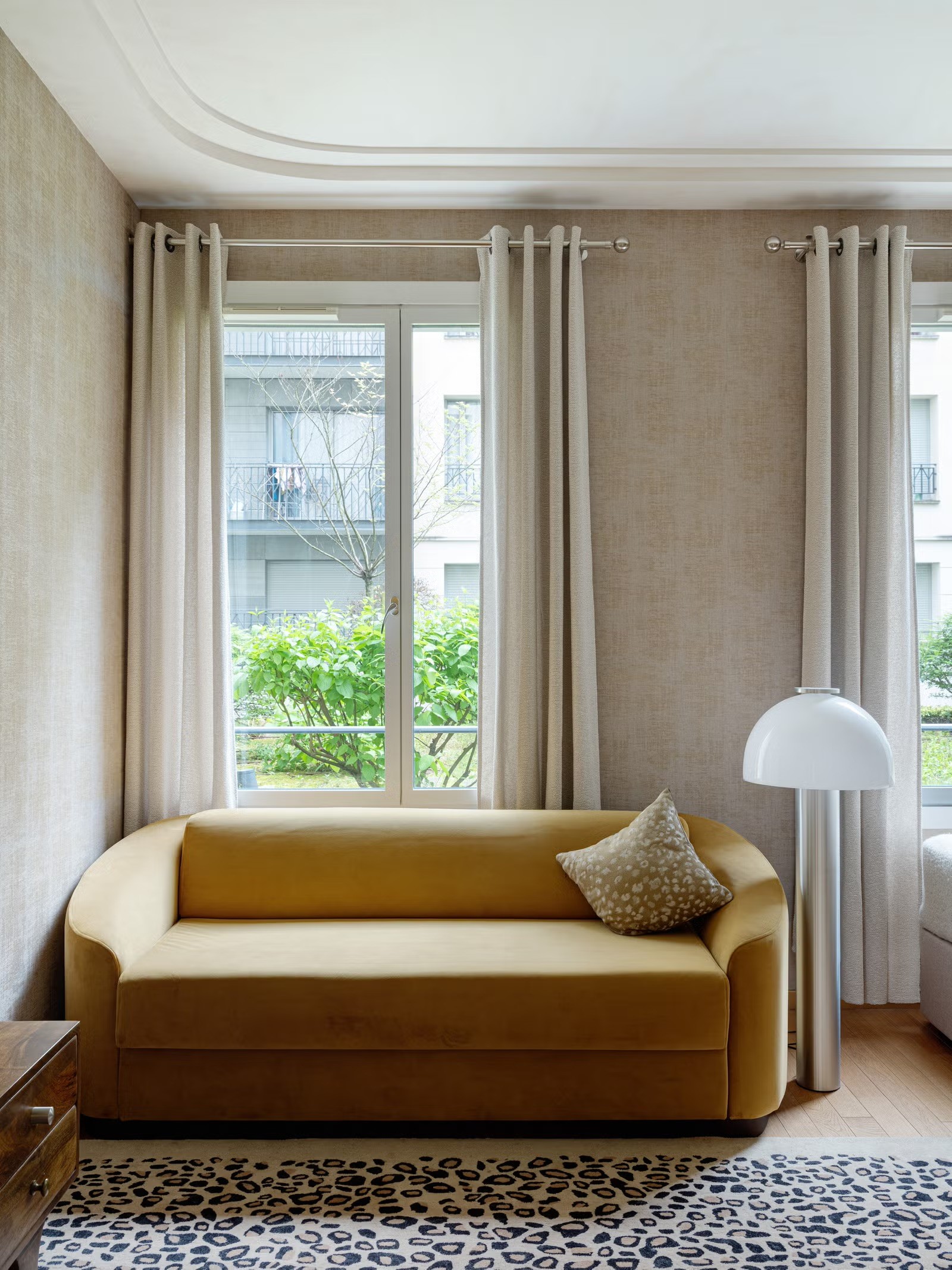 Salon lumineux avec canapé jaune moutarde devant une fenêtre, créant une ambiance de refuge urbain élégant.