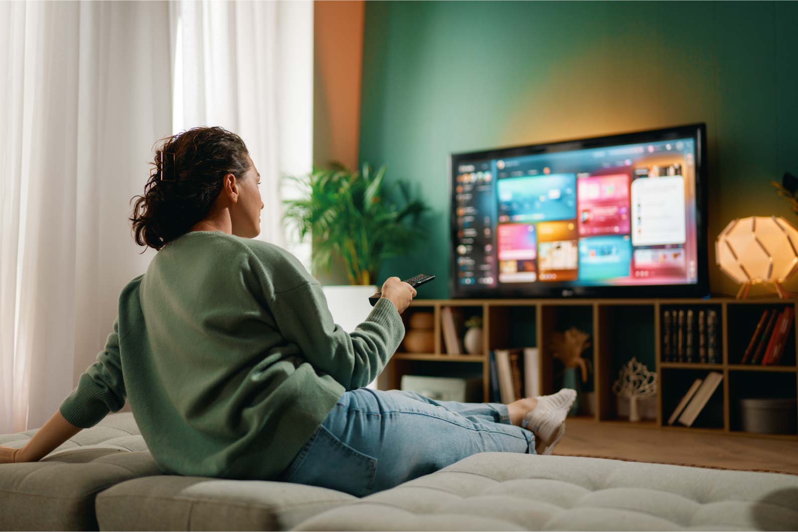 Kobieta siedząca na kanapie z pilotem w dłoni, oglądająca nowoczesną reklamę wideo 3D na dużym ekranie telewizora w domowym salonie.