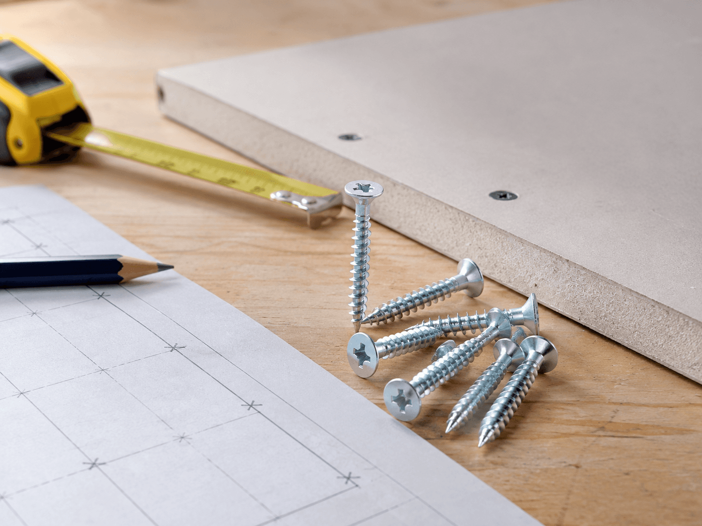 Zinc drywall screws beside gypsum board plans and measuring tape for project quantity planning