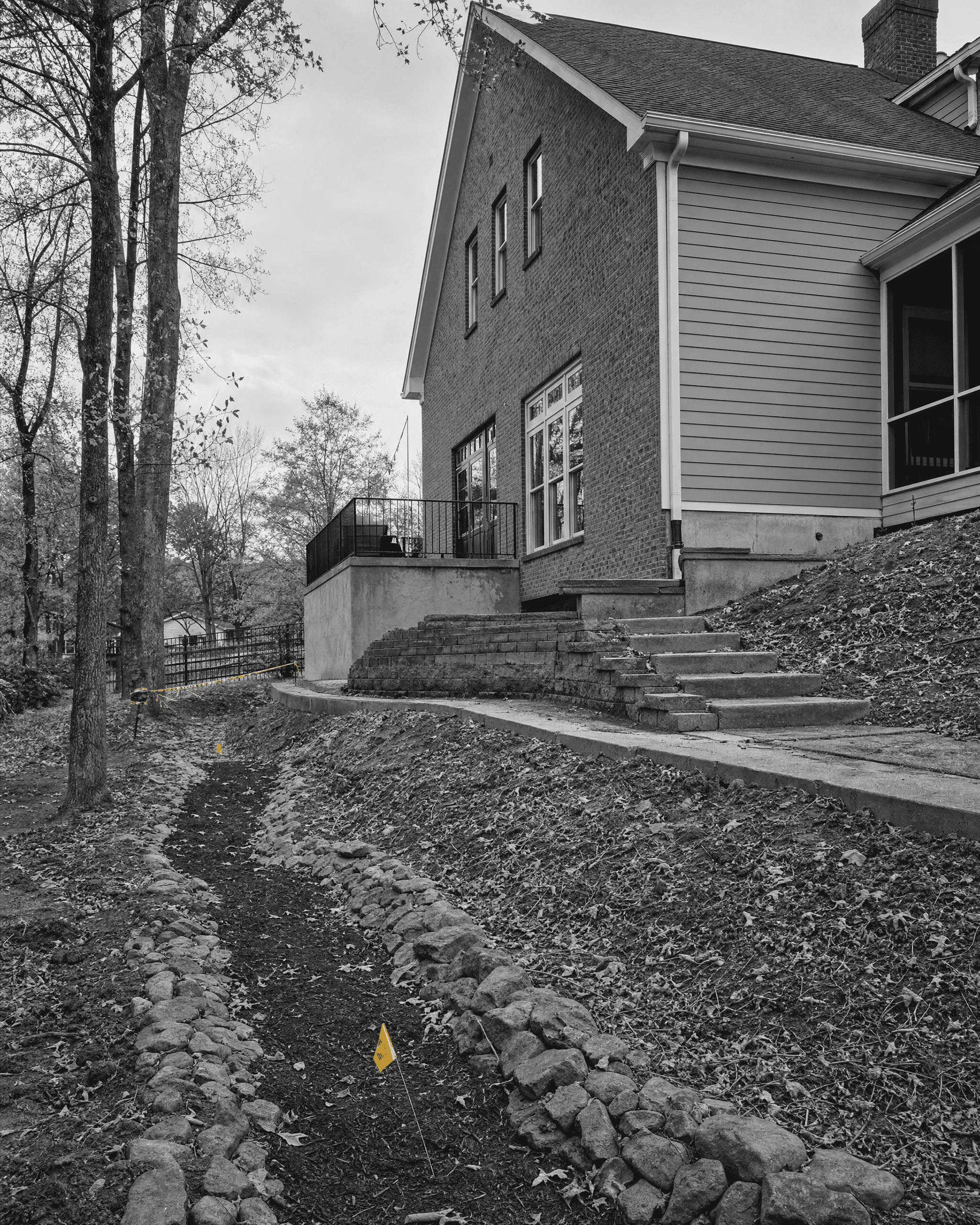 Residential property showing the home, foundation, sloped grade, hardscape, and a stone-lined drainage path along the site.