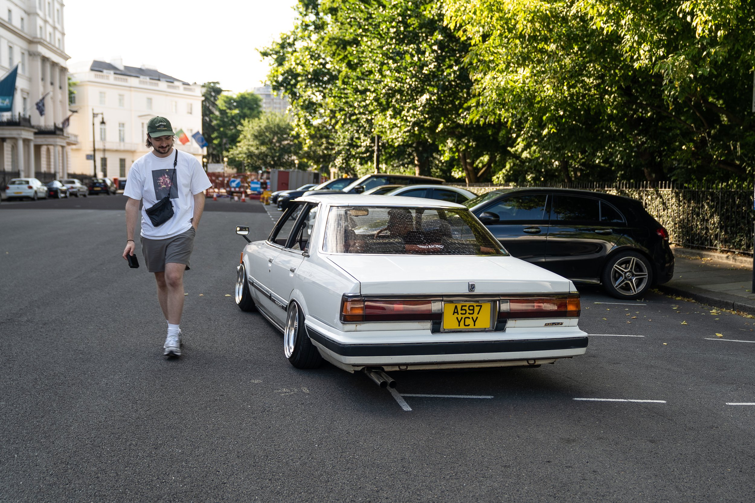 A man with a camera walking next to a white car
