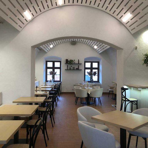 这家餐厅内部充满光线，拱形天花板、木制桌子、软垫椅，以及后部的两个大窗户，营造出一种明亮的氛围。