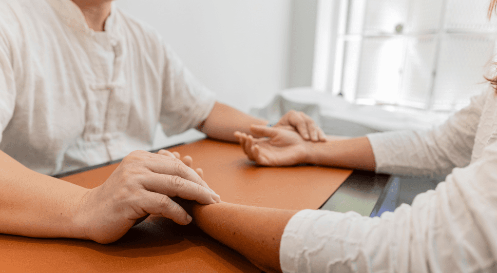 Image of two people holding hands across a table with a window in the background