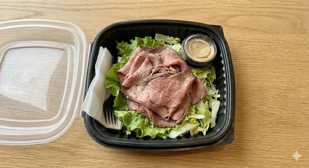 A top-down view of an Arby's roast beef entree salad with a stack of thin-sliced roast beef over green leaf lettuce, in a black plastic takeaway bowl with a side of Horsey Sauce.