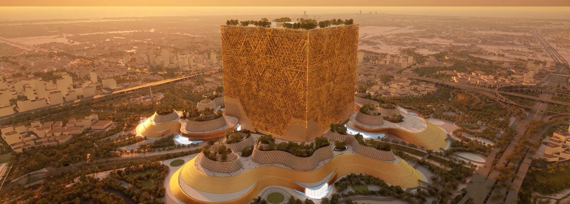 لقطة جوية لمبنى المكعب العملاق في حي المربع الجديد محاطاً بالمباني ذات الأسطح المتموجة والحدائق الغناء وقت الغروب، كأضخم داون تاون حديث في العالم بقلب الرياض.