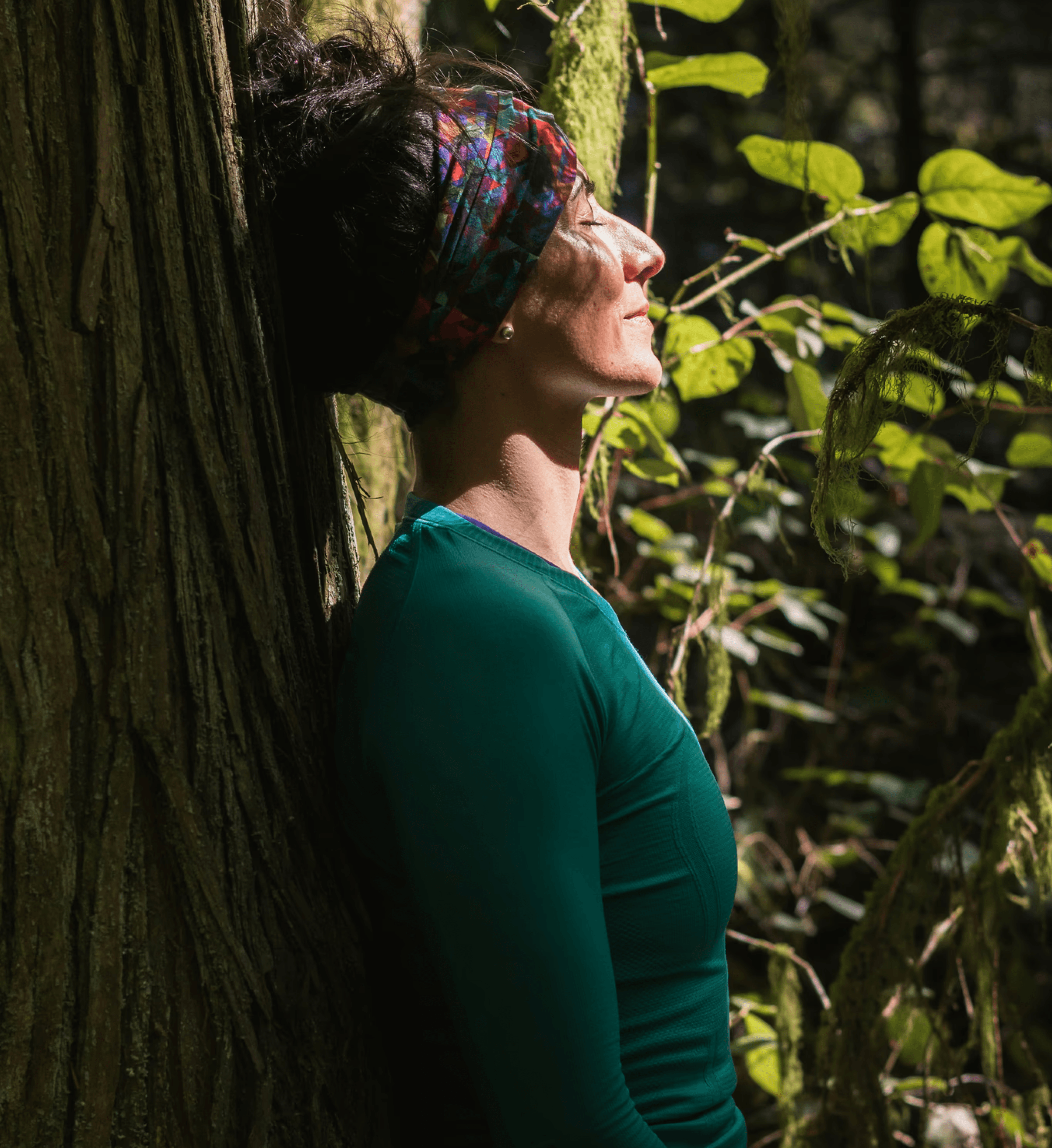 A person leans against a tree, smiling and enjoying the serene atmosphere of a lush green forest.