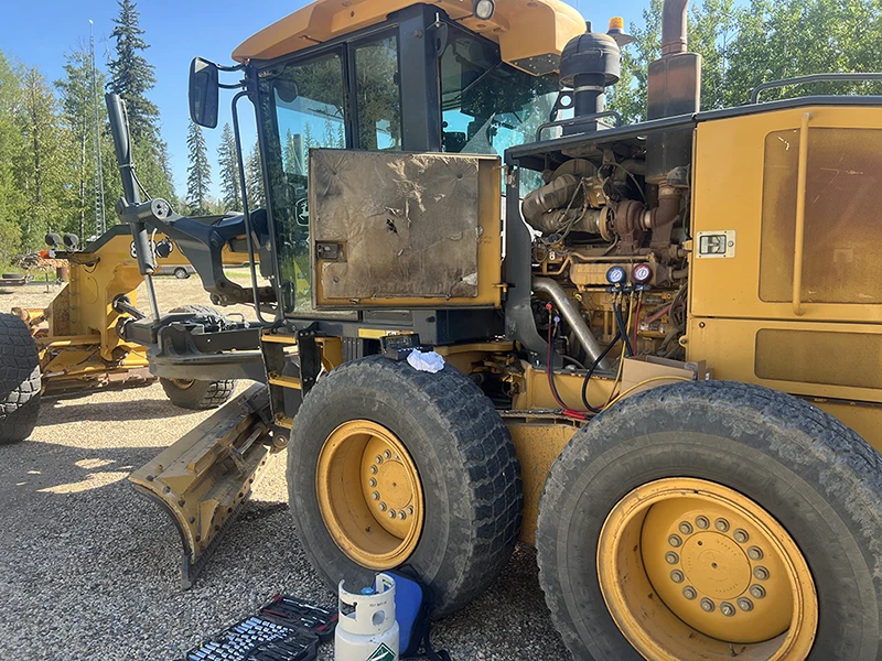 HVAC technician servicing air conditioning system on a heavy-duty road grader at a job site
