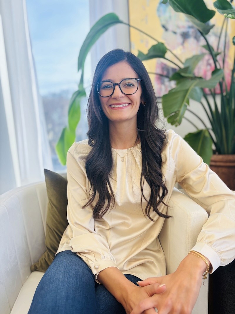 A young person with long, wavy hair sits in front of a plain background, looking directly at the camera.