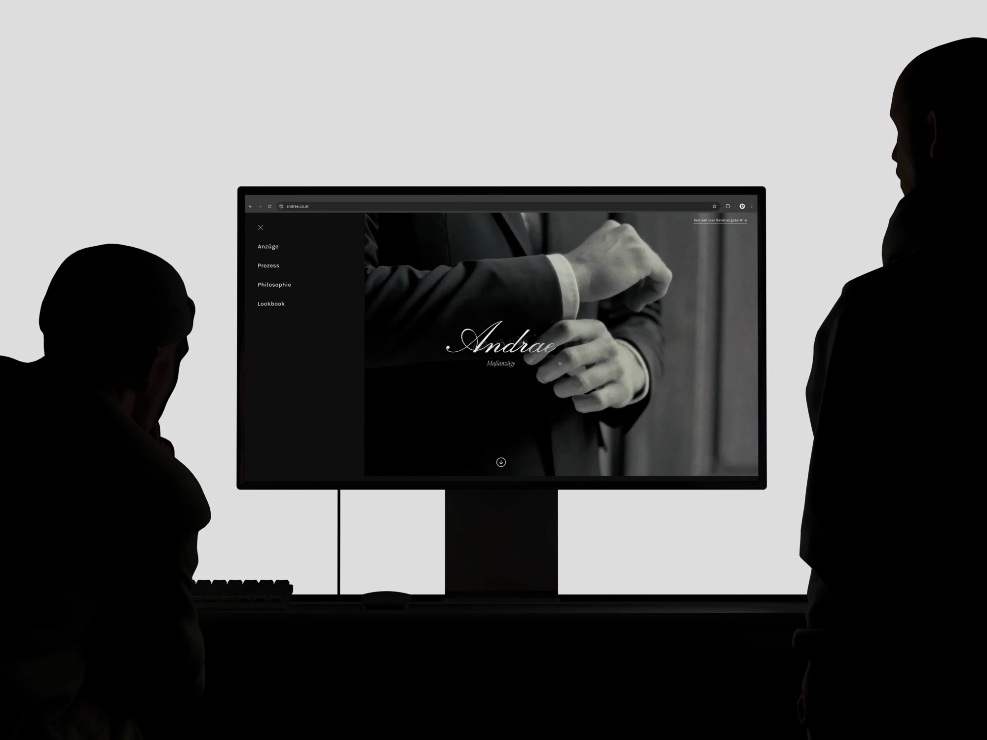 Ein Bild von einem großen Bildschirm welcher die Homepage von Andrae Maßanzüge zeigt. Davor sieht man schwarze Silhouetten von zwei Personen.