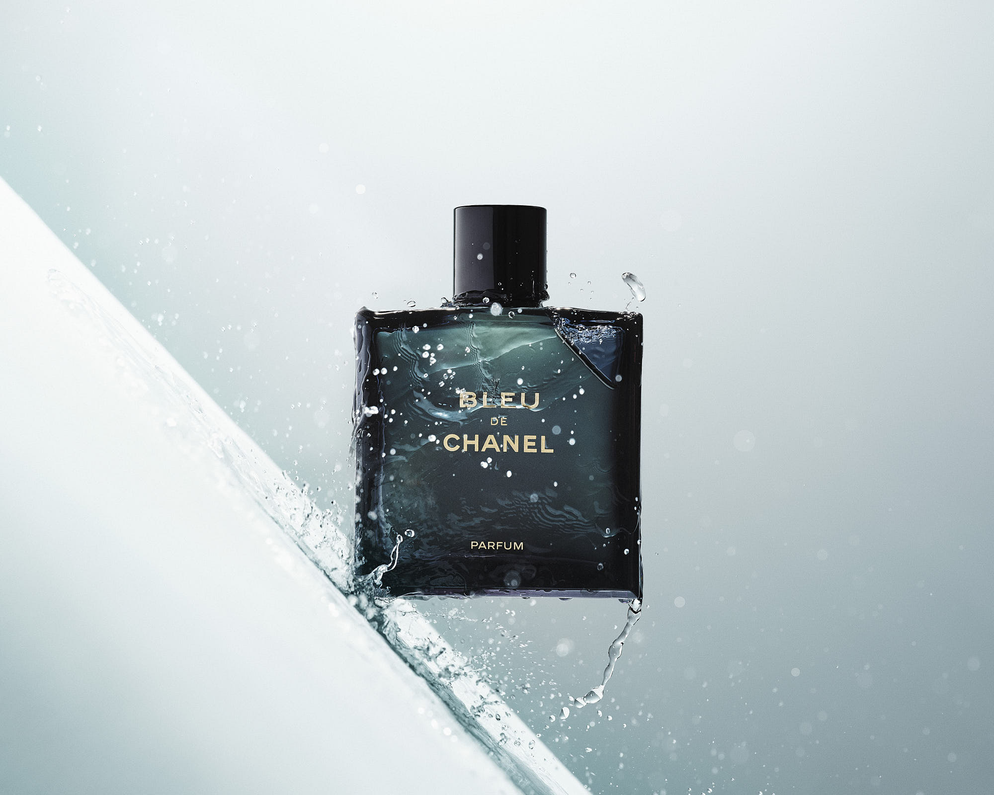 A sleek black perfume bottle placed on a reflective surface with a soft, light background.