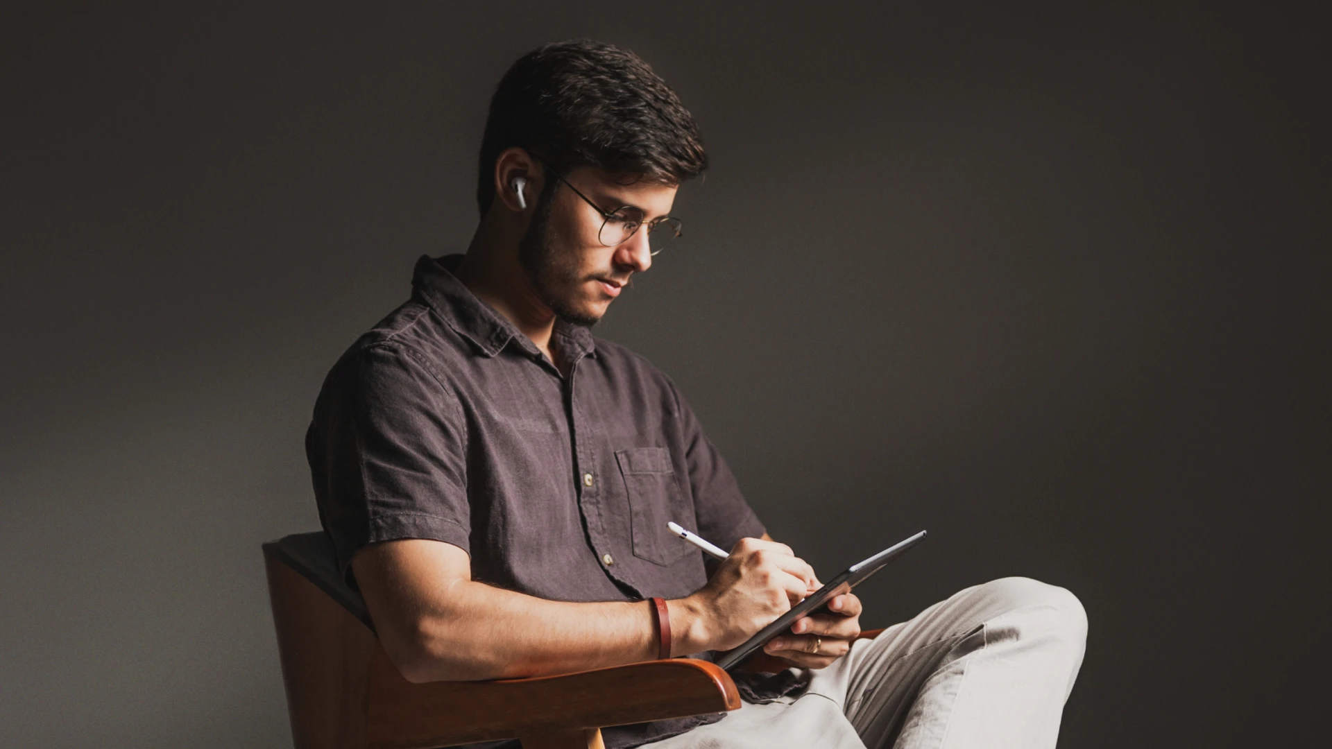 A spacious industrial-style interior with exposed brick walls, large windows, and natural light pouring in during sunset. Wooden desks with plants and workspace materials are arranged along the walls, with a view of greenery and an outdoor seating area.