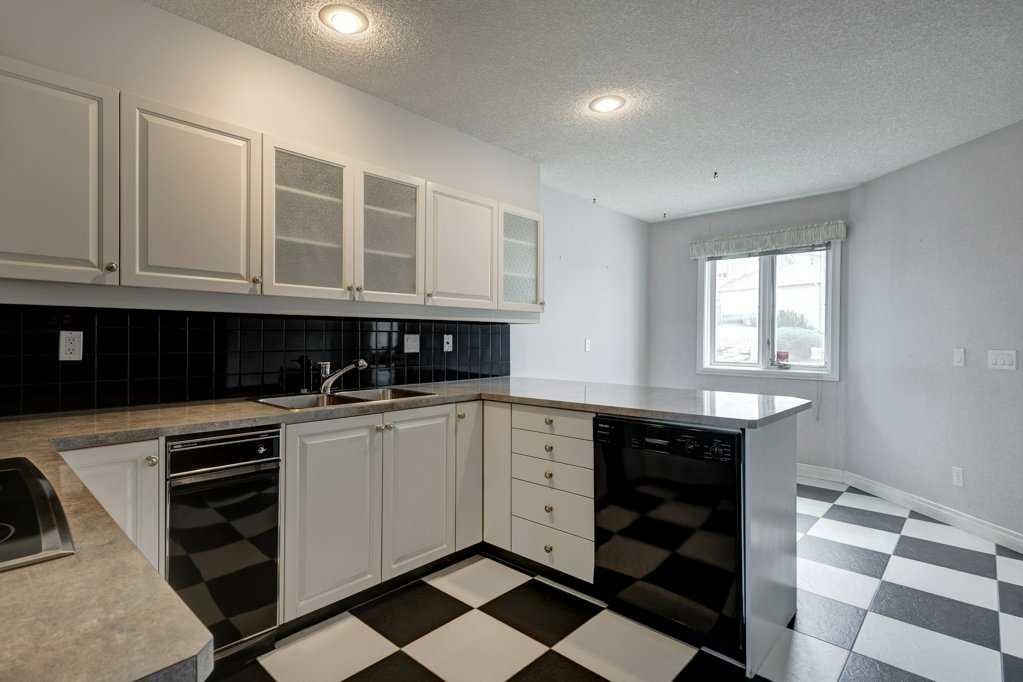Strathcona kitchen before renovation: dated white cabinets, black tile backsplash and checkerboard floor