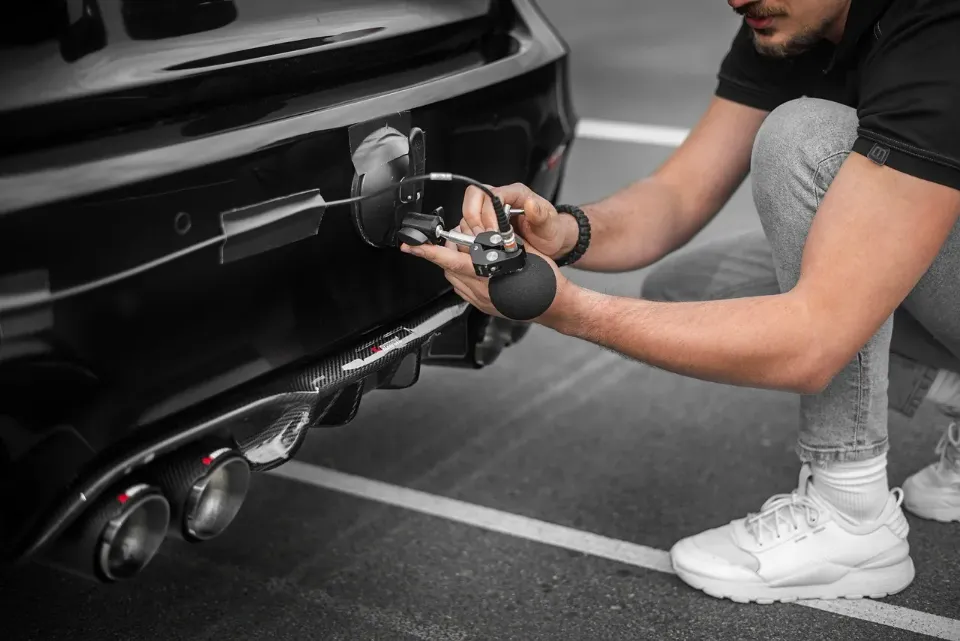 Man uses a device on a black car's bumper near exhaust pipes.
