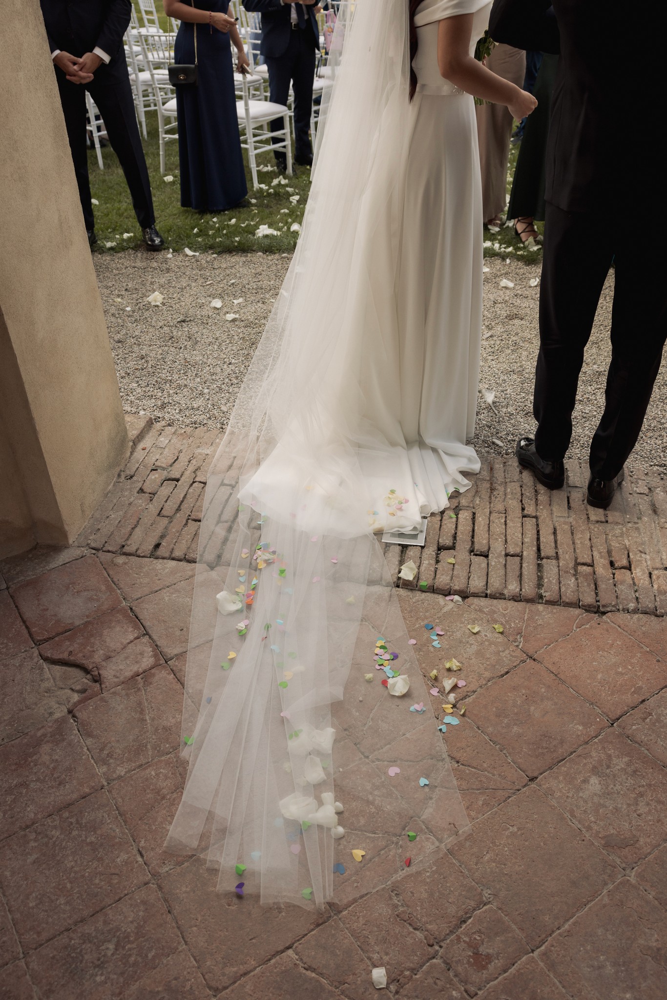 Sposa con velo lungo e bouquet bianco cammina su pavimento in laterizio verso la cerimonia a Villa Negri