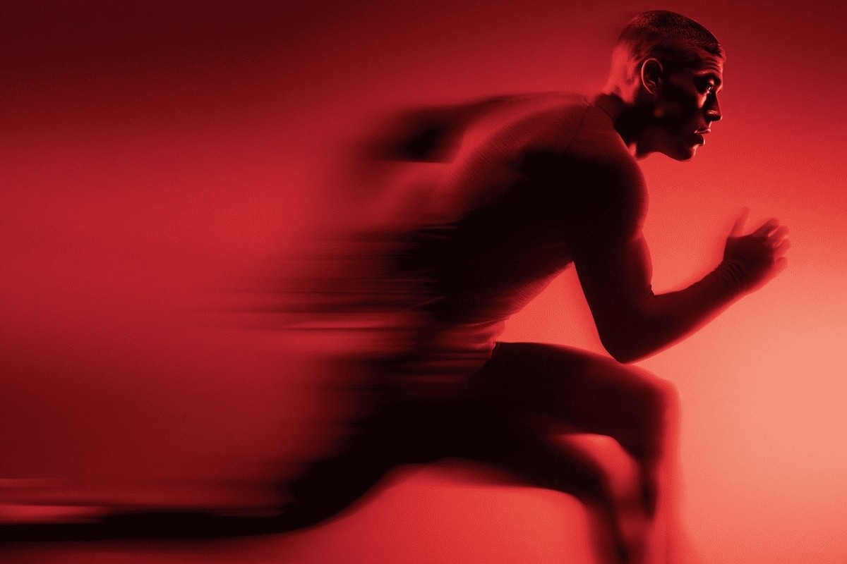 A blurred, dynamic side profile of a man in motion, portrayed against a vibrant red background to emphasize speed and energy.