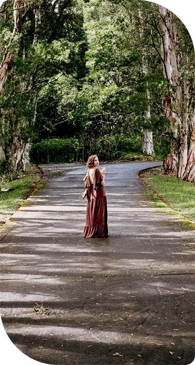 Woman walking down a mystical tree-lined path surrounded by ancient oaks draped in Spanish moss, symbolizing the transformational journey and hero's quest
