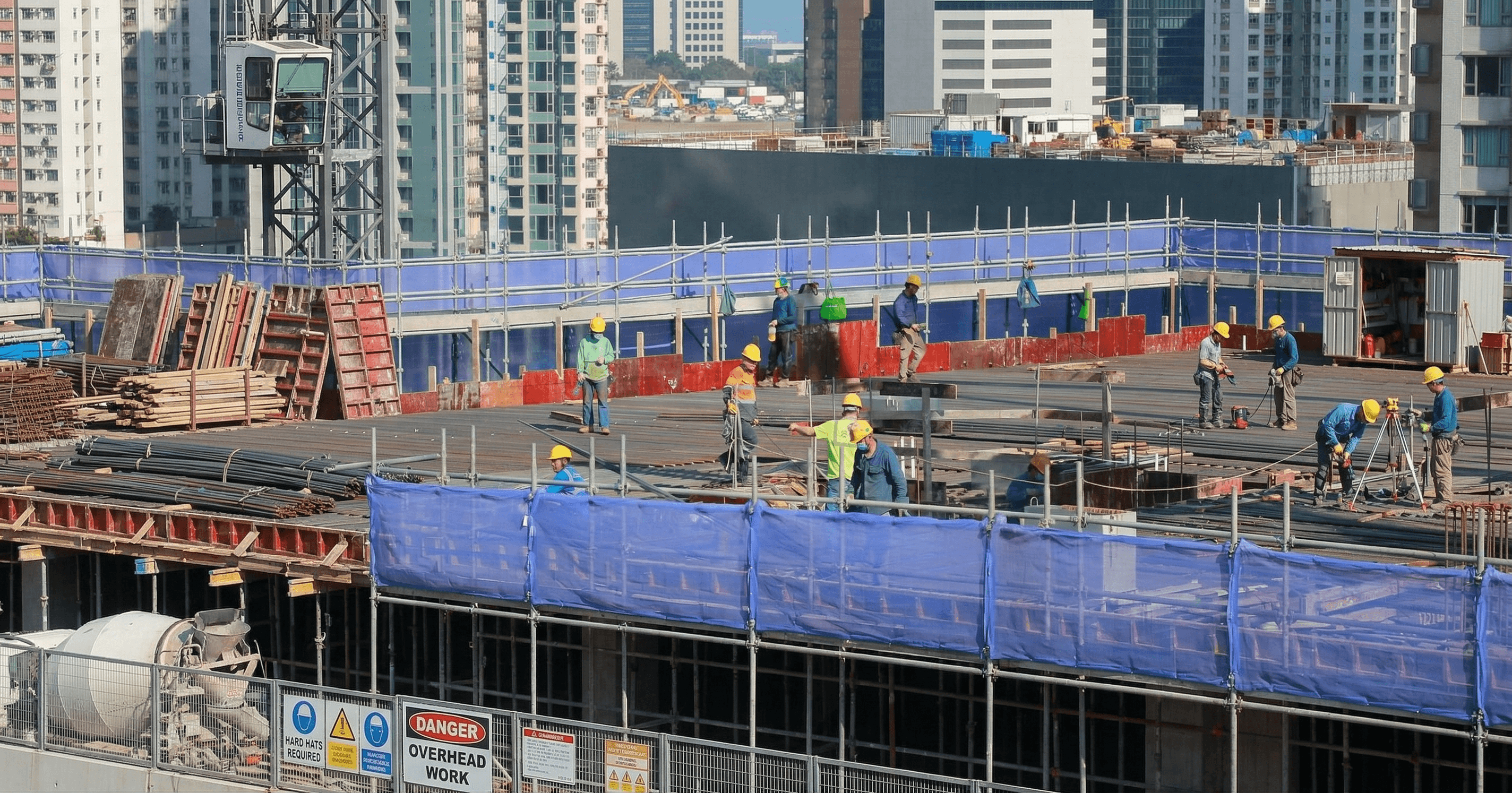 香港建築地盤施工現場，工人佩戴安全裝備作業，背景為市區高樓，對應建築工程全險及勞工保險保障。