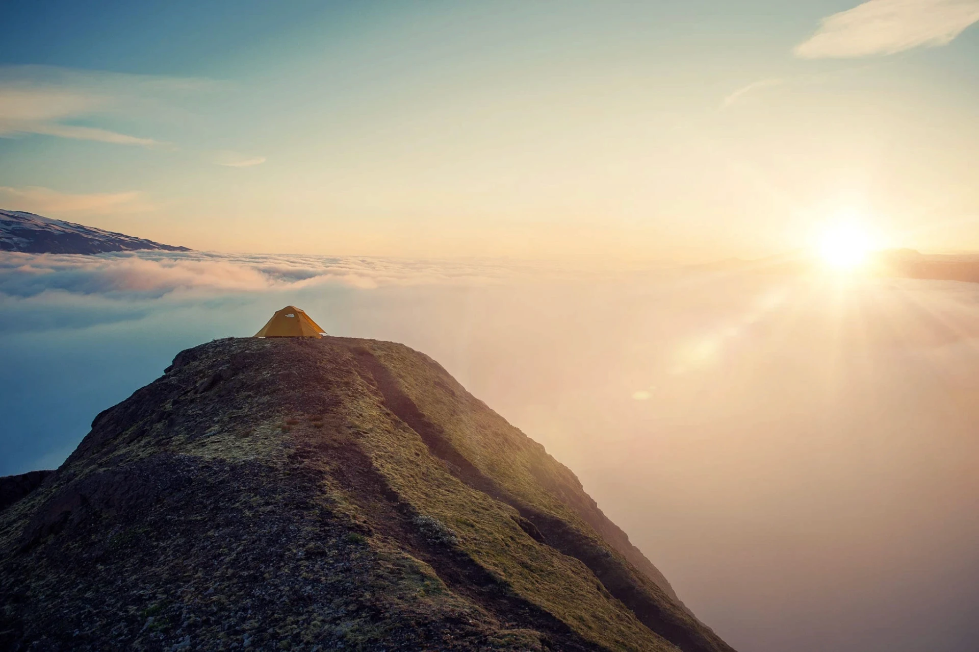 Small tent on a mountain ridge above a sea of clouds at sunrise.