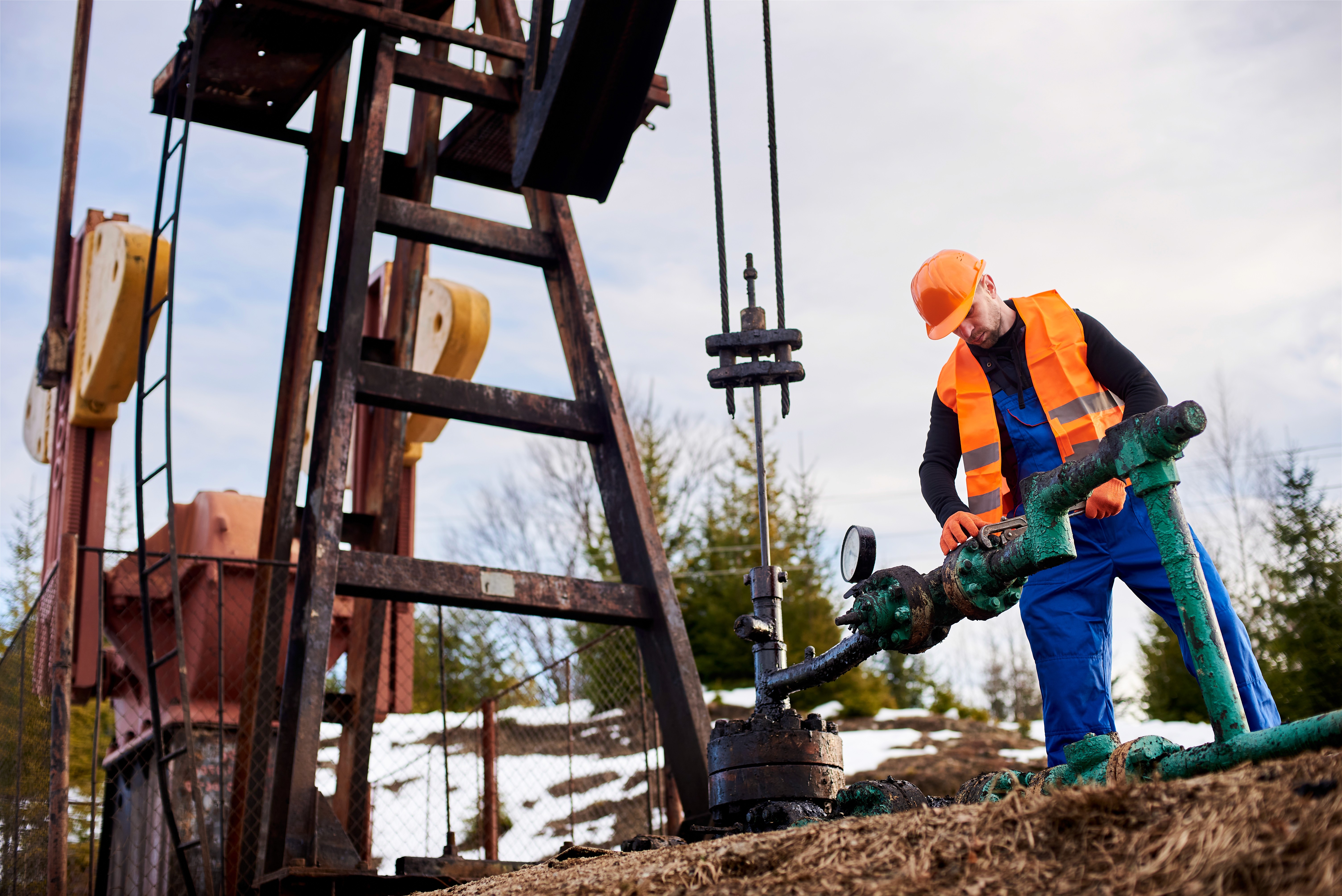 Oilfield worker using pipe wrench on an oil pump jack.
