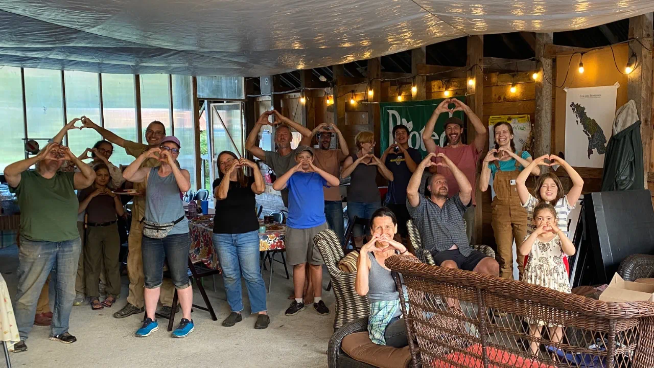A group of adults and children standing together indoors, making heart shapes with their hands.