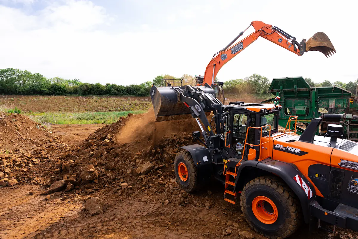 Excavator loading soil on UK construction site during controlled demolition and bulk excavation project