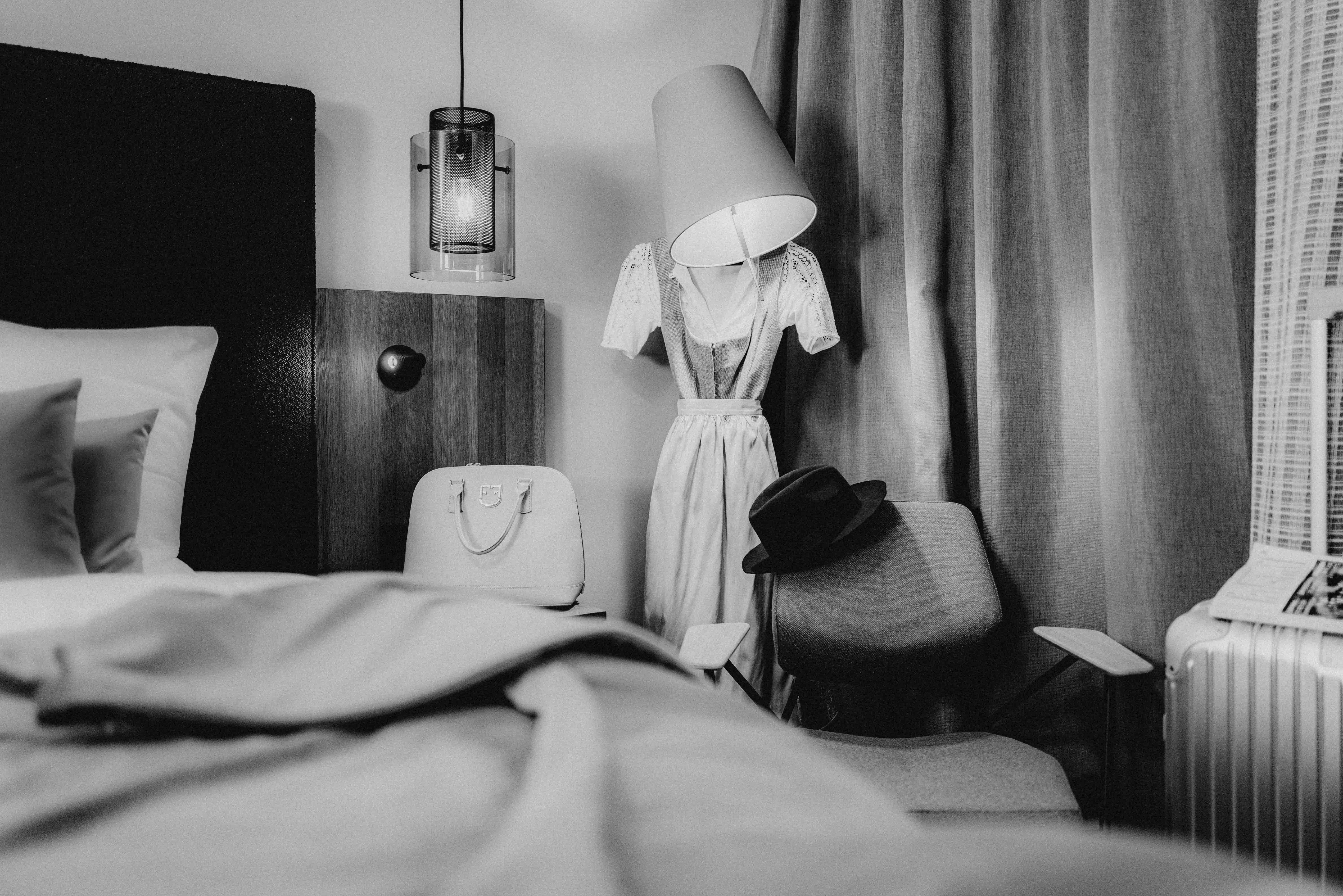 A cozy hotel room featuring a bed, lamp, and curtains in black and white tones.