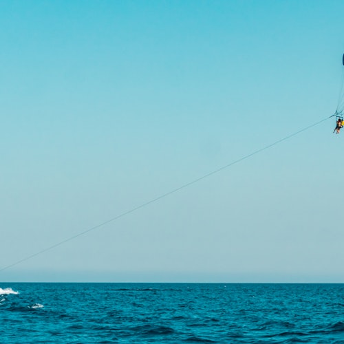 Person parasailing over the ocean under a clear blue sky, connected by a long rope from a boat.