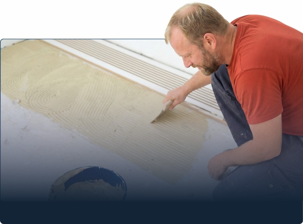 Mann verteilt Kleber auf einer Untergrundplatte.