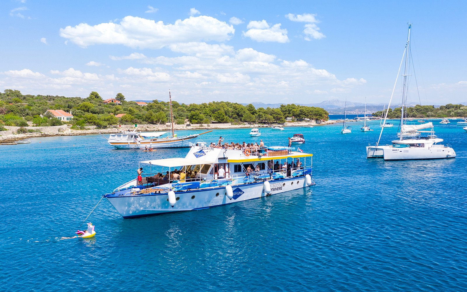 Cruise ship with tourists in Split's Blue Lagoon, surrounded by sailboats and clear blue water.