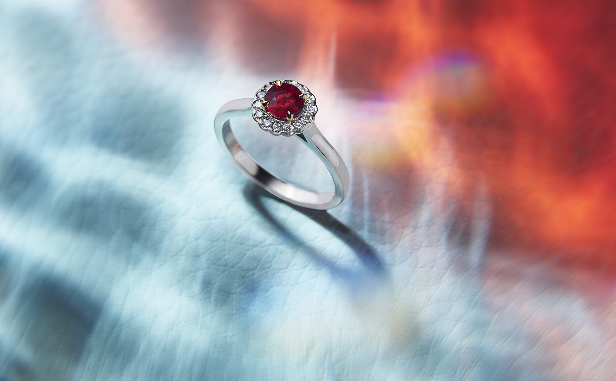 Elegant silver ring with red gemstone and diamonds on colorful background.