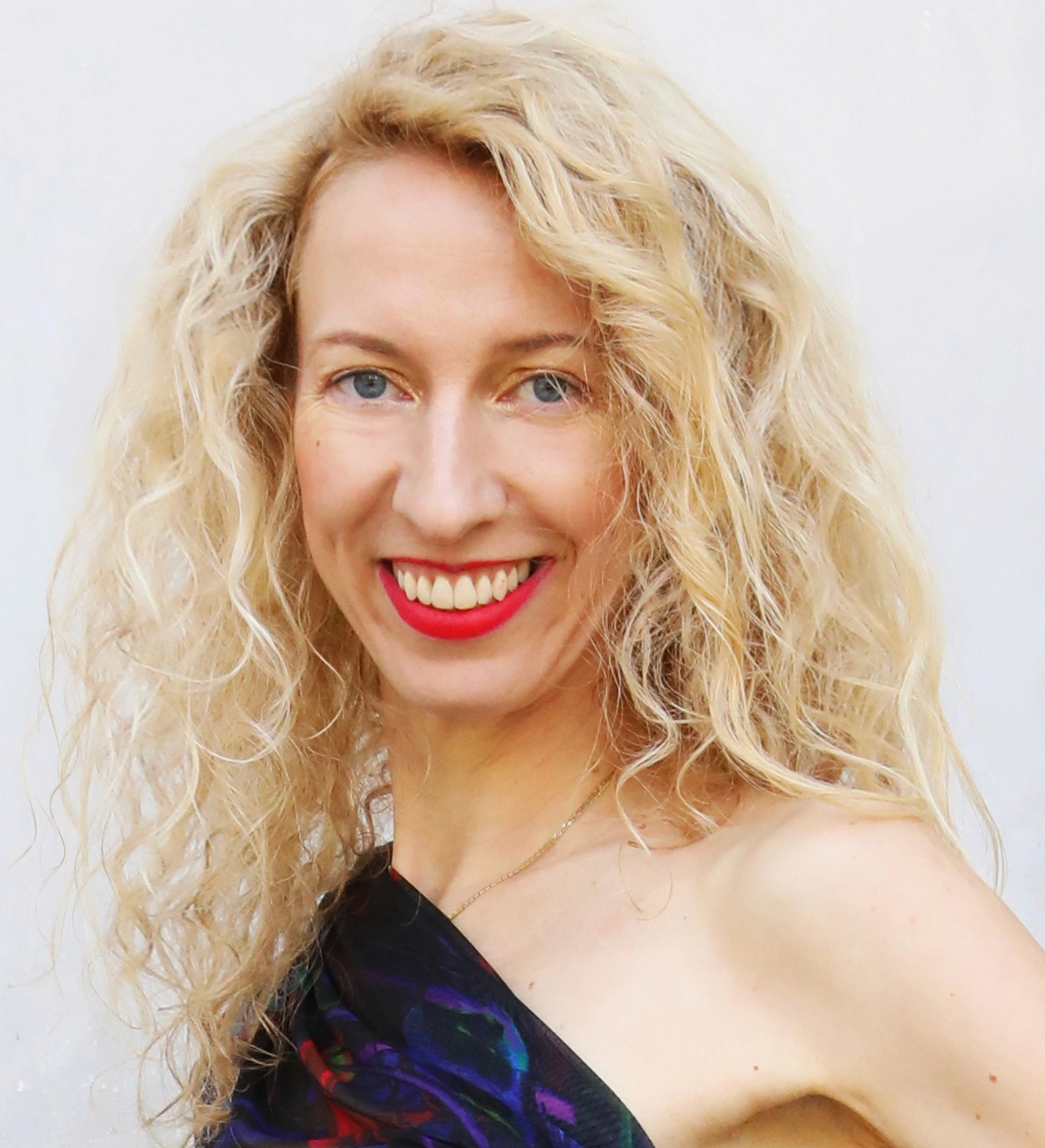 Person wearing a blue puffer jacket and red backpack standing in front of a light blue building on a city street.