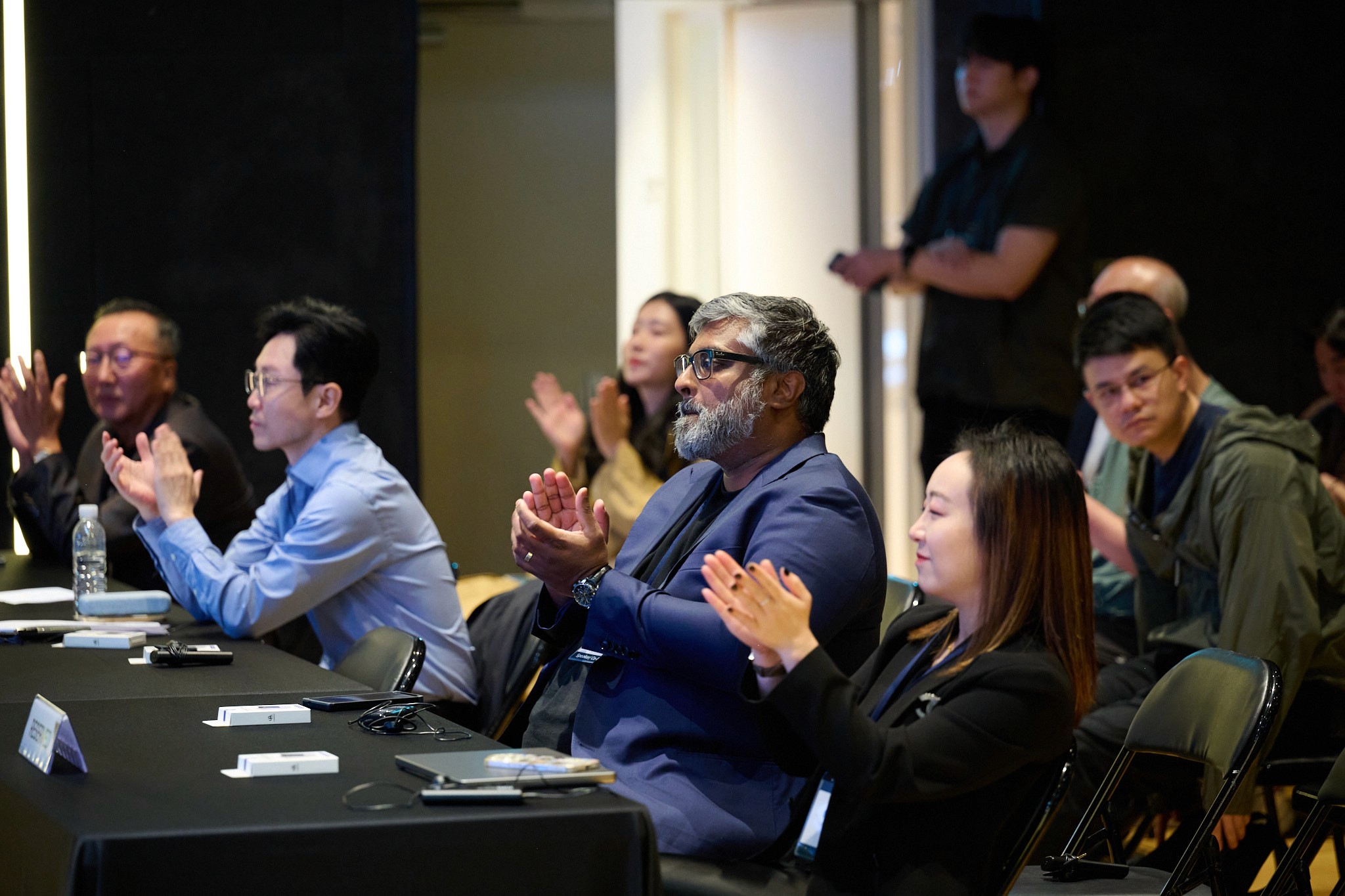 person discussing while standing in front of a large screen in front of people inside dim-lighted room