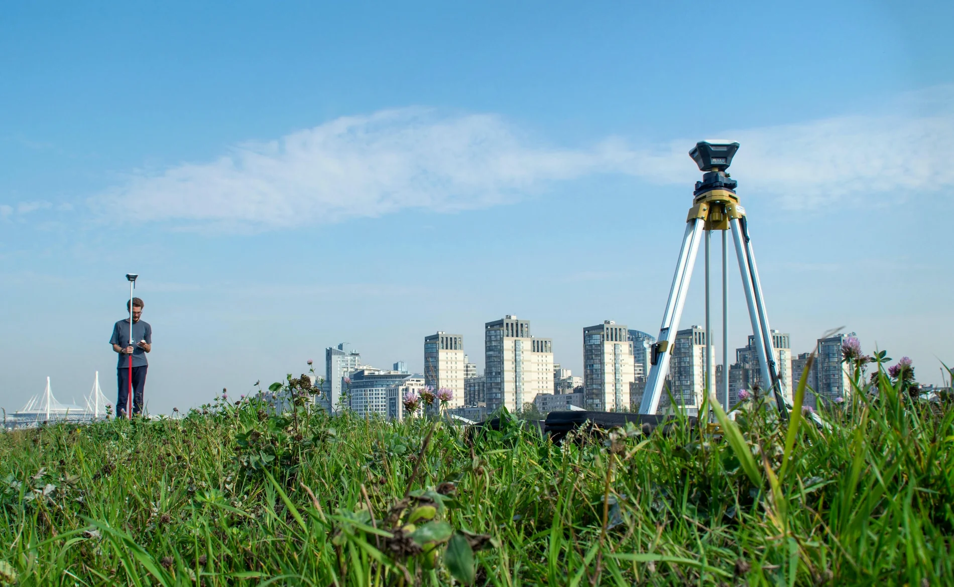 Surveyor operating a rover with a base station in the foreground during an urban GPS survey.