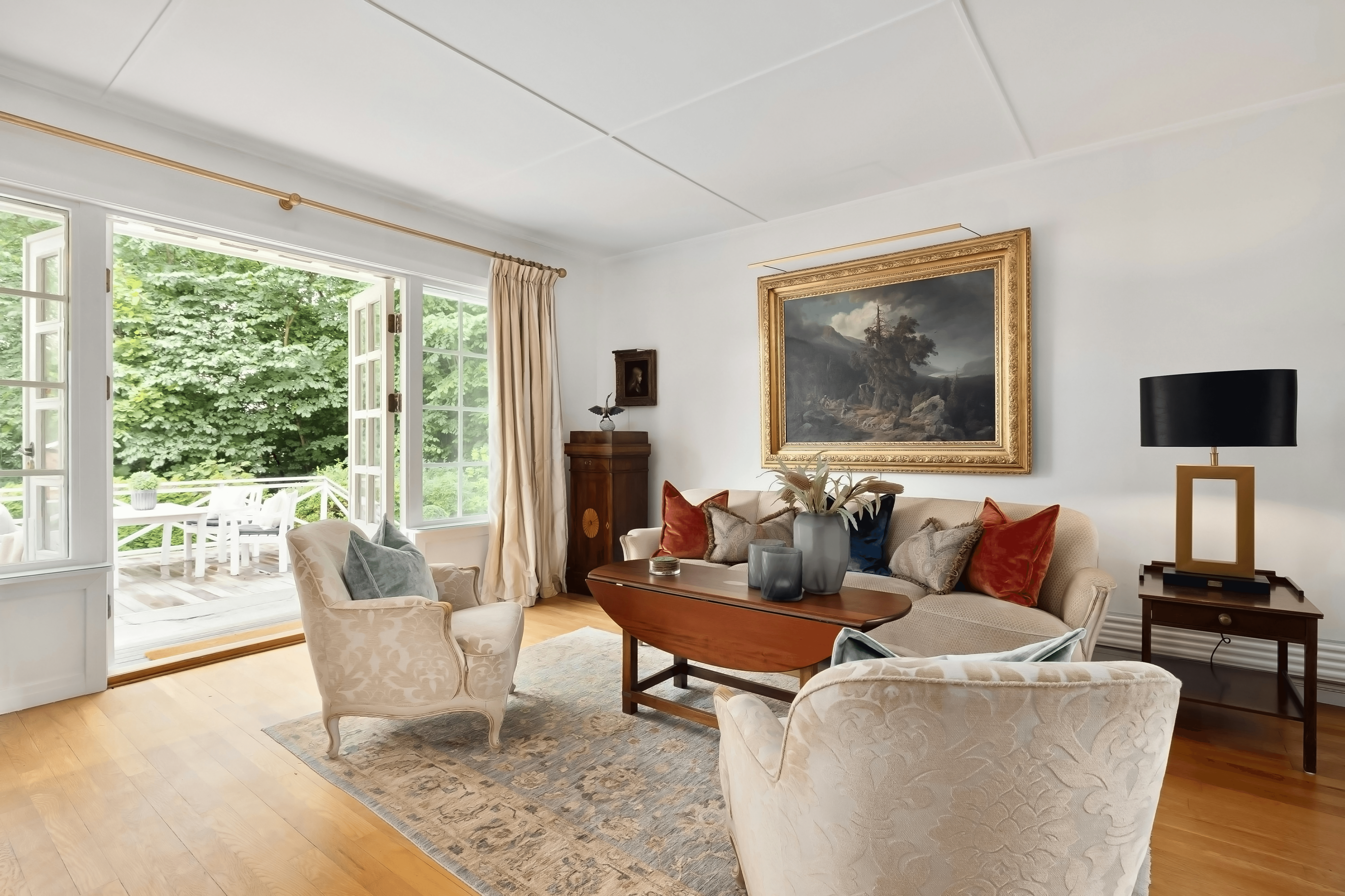 Traditional living room with gold-framed landscape painting, velvet cushions, and garden French doors