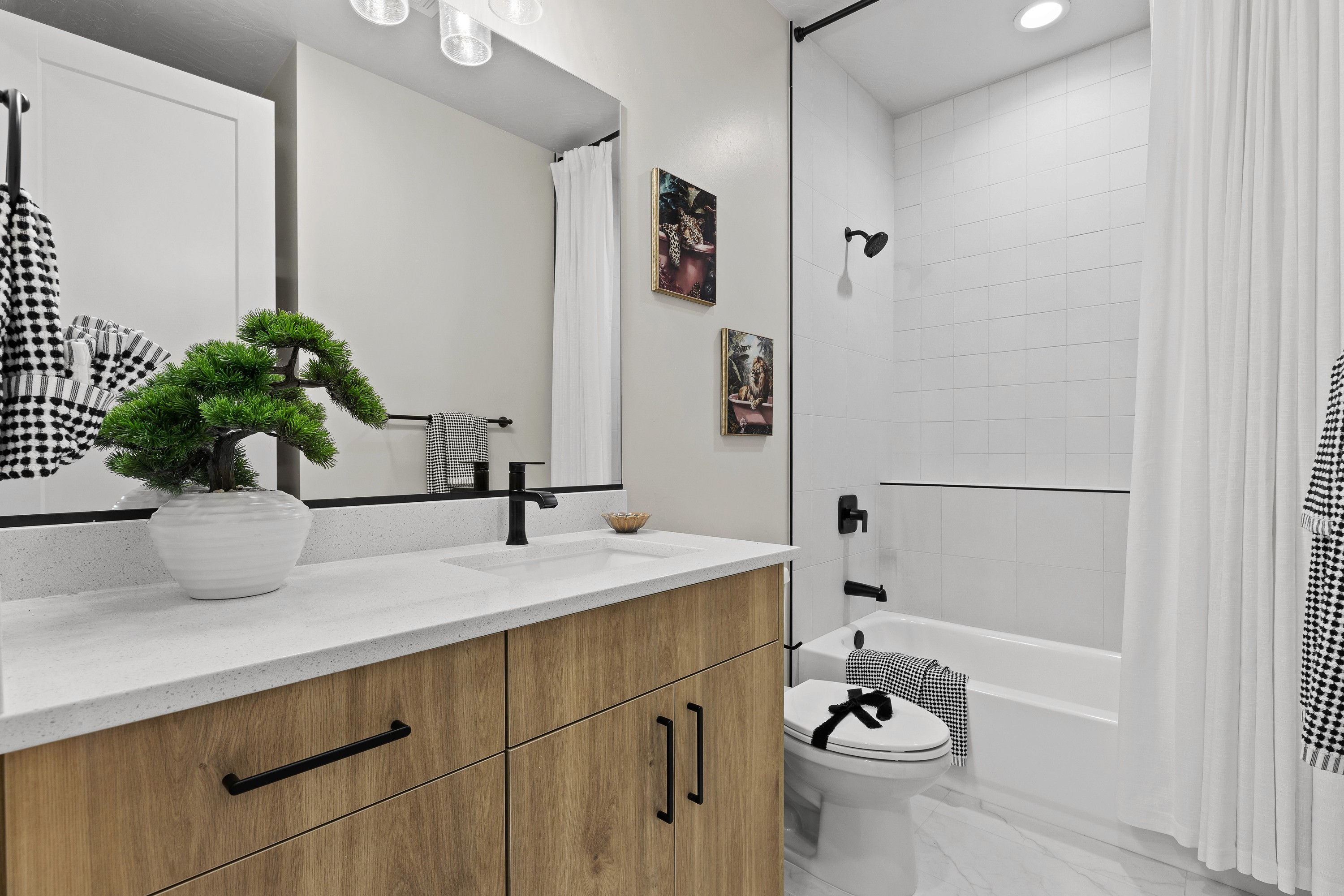 Alt text: "Bathroom in a custom home in Hurricane, Utah featuring wood cabinetry, white quartz countertop, black fixtures, and a tiled shower and tub combination.