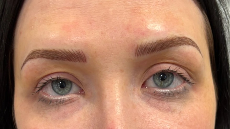 Front-facing view of a woman’s face showing fresh microblading results with crisp, hair-like strokes and a balanced brow shape.