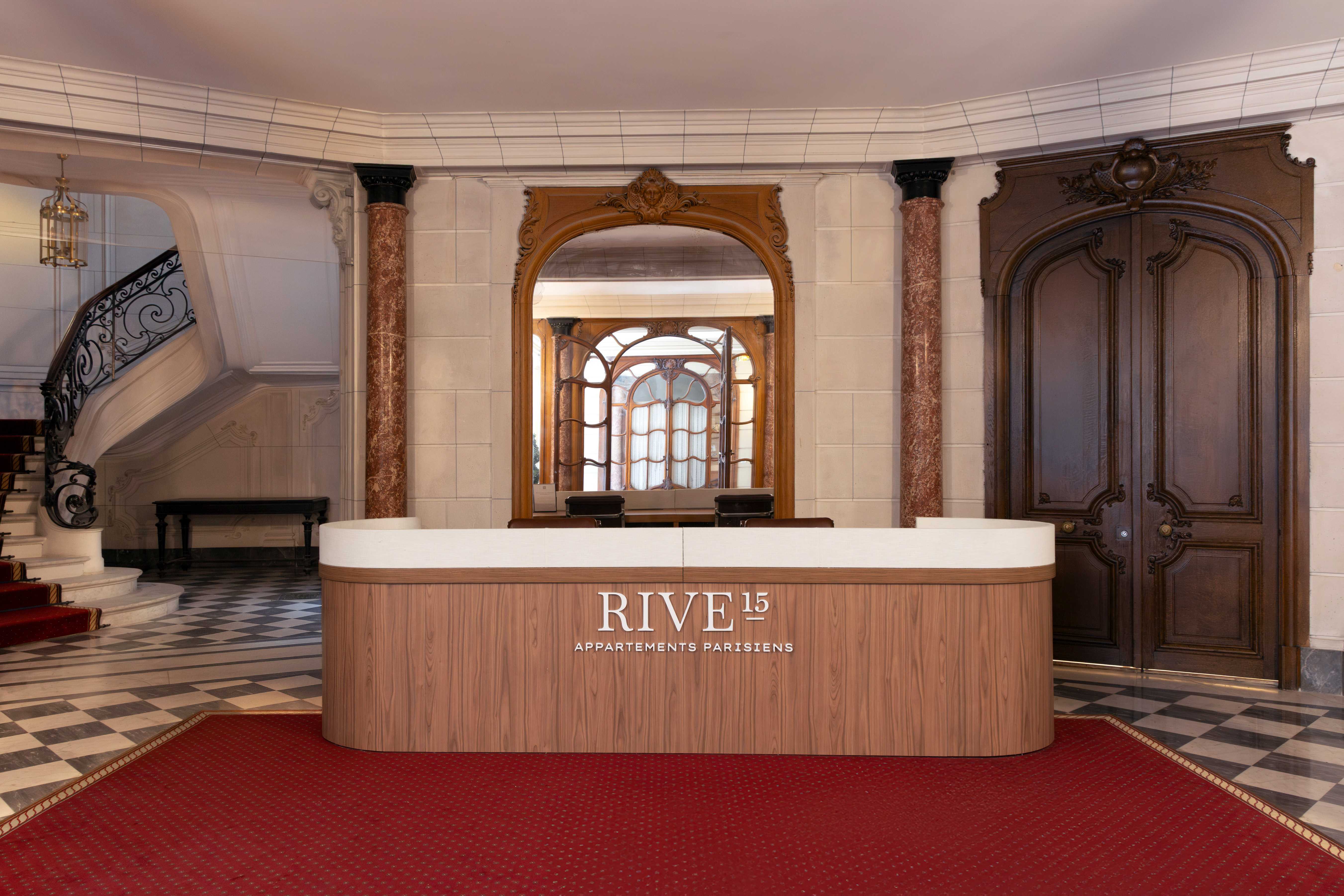 Hall de réception Rive 15 avec comptoir en bois, tapis rouge, miroir doré et porte sculptée
