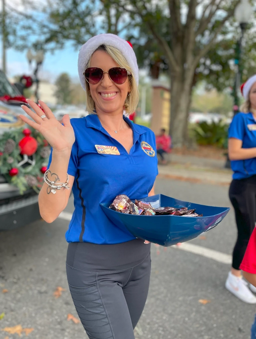 Mrs. Millan wearing a Santa Claus hat waving at the camera.
