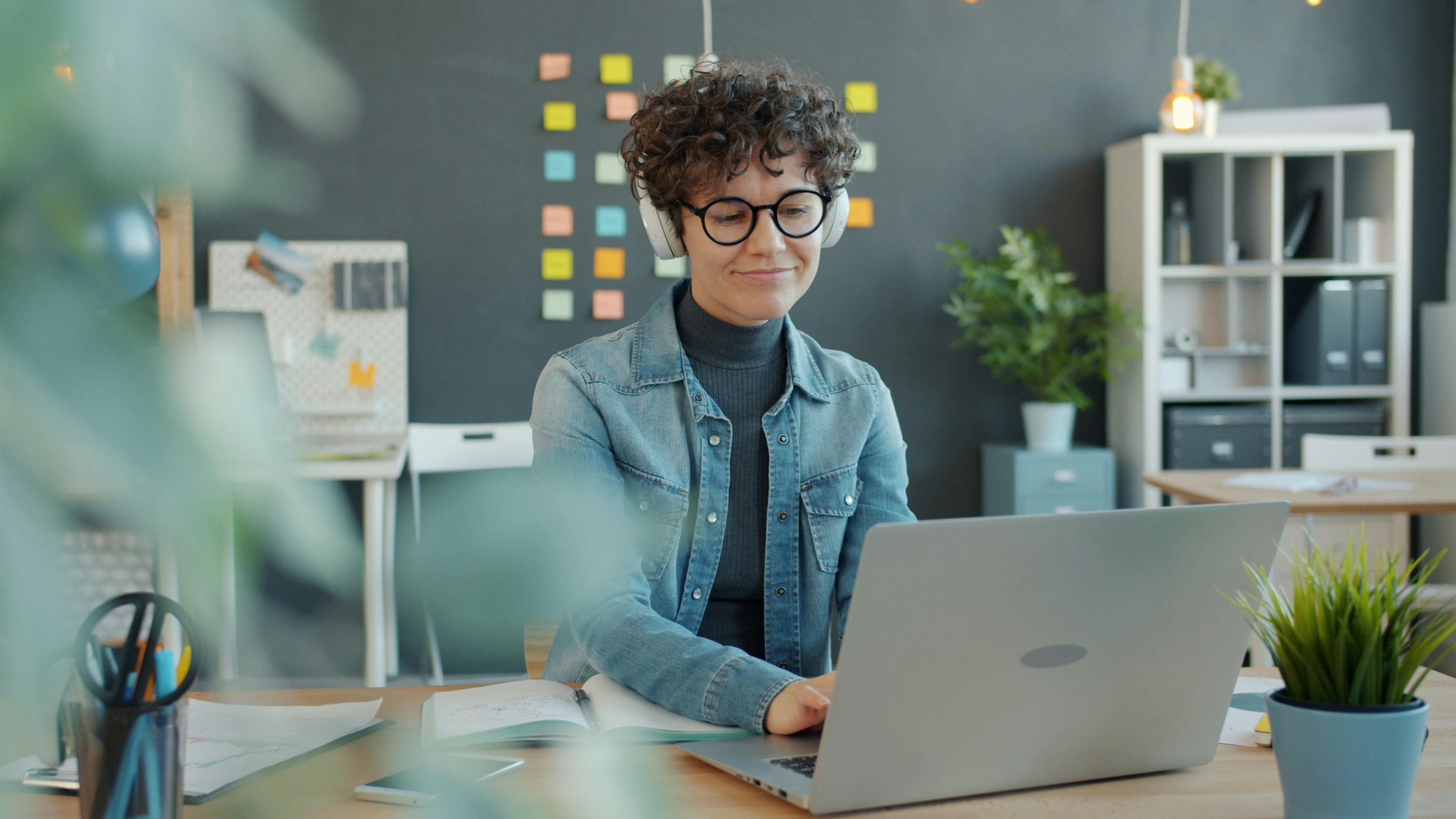 Young woman with headphones working on laptop in office