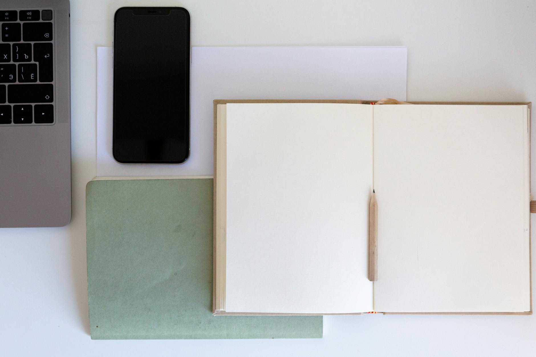 An overhead shot of a laptop, a digital notebook, and a smartphone arranged on a clean wooden desk.