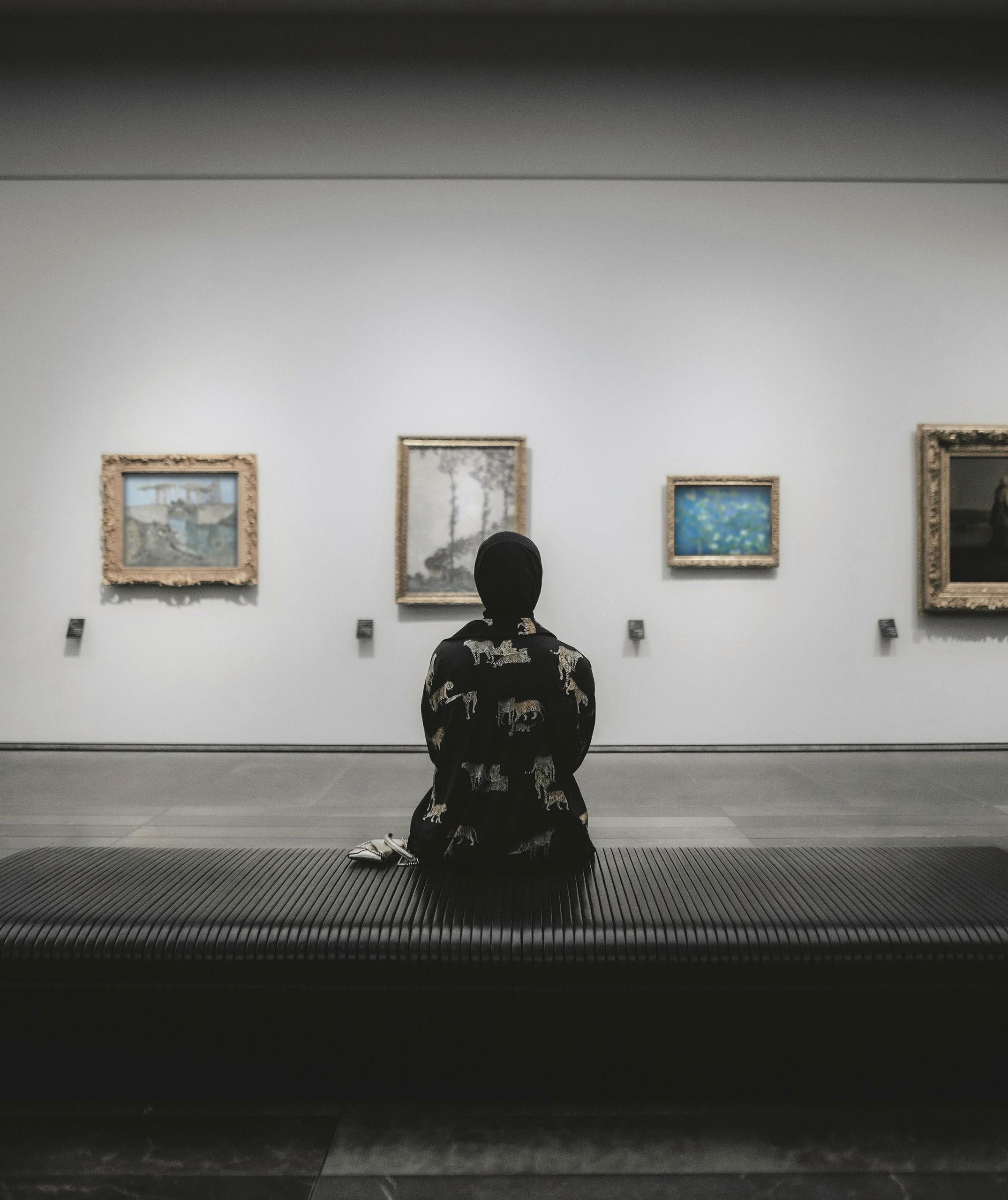 Abstract foreground framing a visitor viewing paintings in a contemporary art gallery
