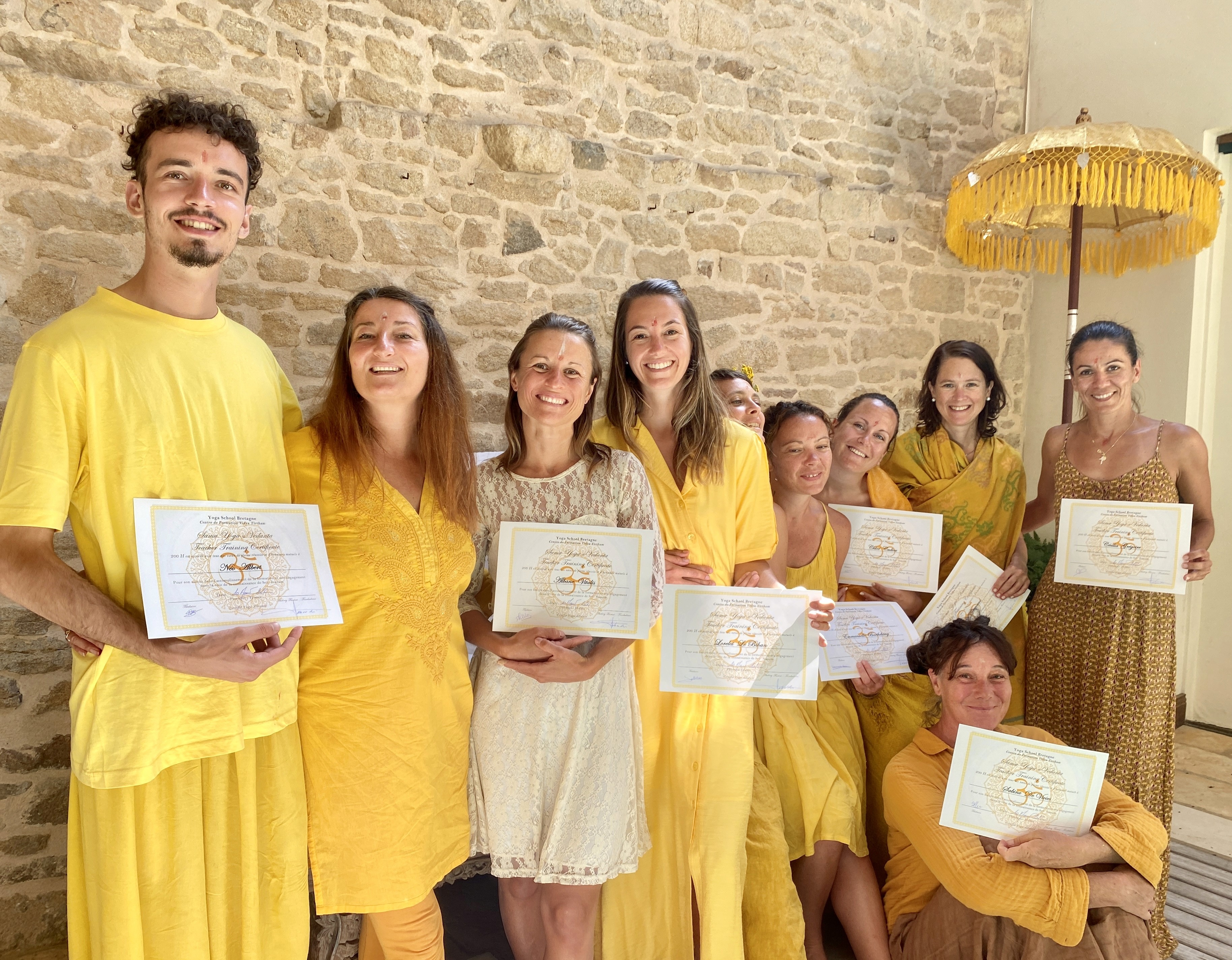Personnes souriantes en vêtements jaunes avec diplômes, célébrant une certification.