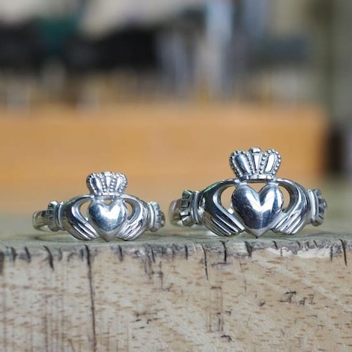 Two silver Claddagh rings with heart, crown, and hands designs displayed on a wooden surface.