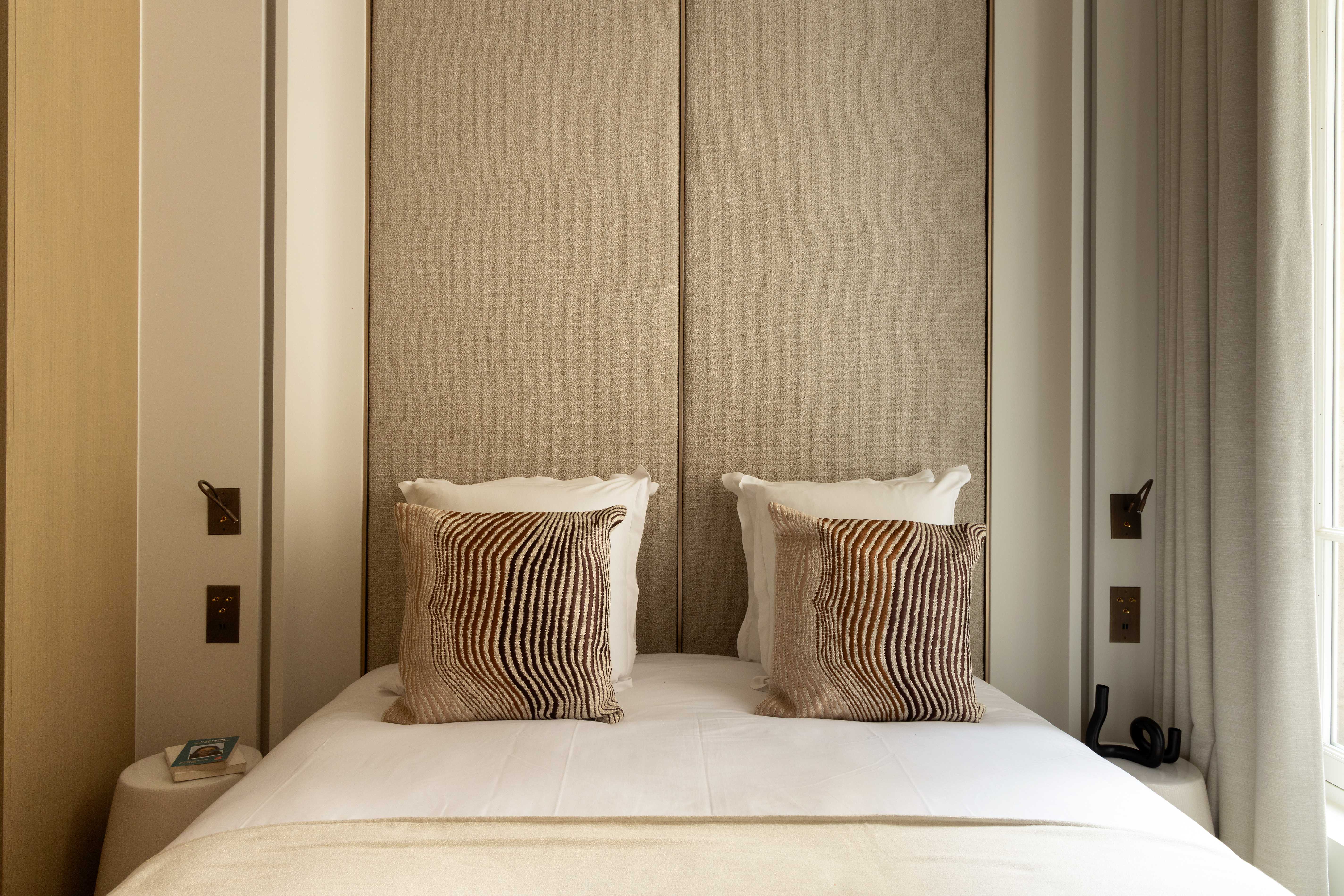 Lit double avec tete de lit textile sable, coussins a motifs ondules beiges, appliques et linge blanc