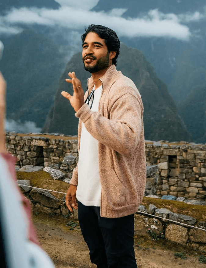 Smiling young man with short hair poses against a dark background, wearing a green button-up shirt.