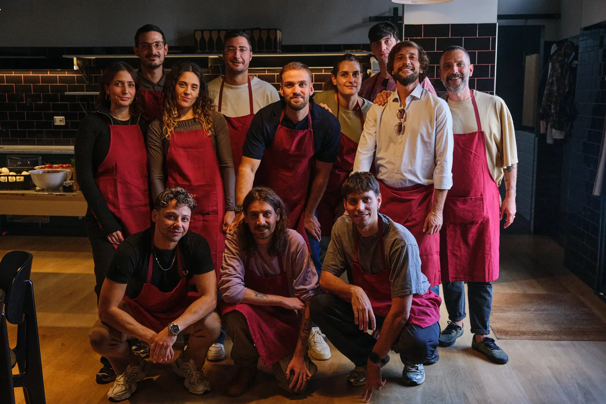Foto di gruppo: il team di Reka con i grembiuli rossi nella cucina di Casa Fluviale, Roma, durante il team building aziendale.