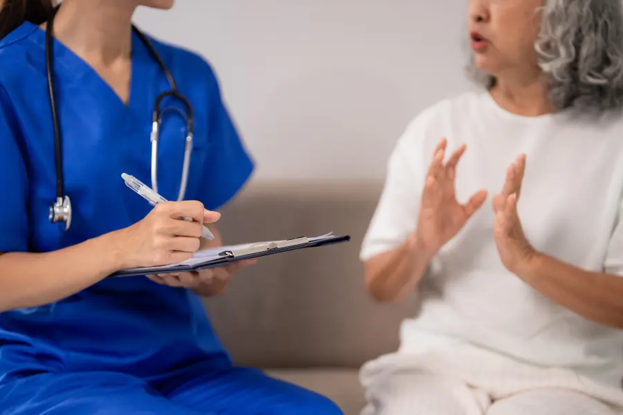 Nurse using AI medical consultant software to document symptoms as an elderly patient describes her condition during a clinical assessment.