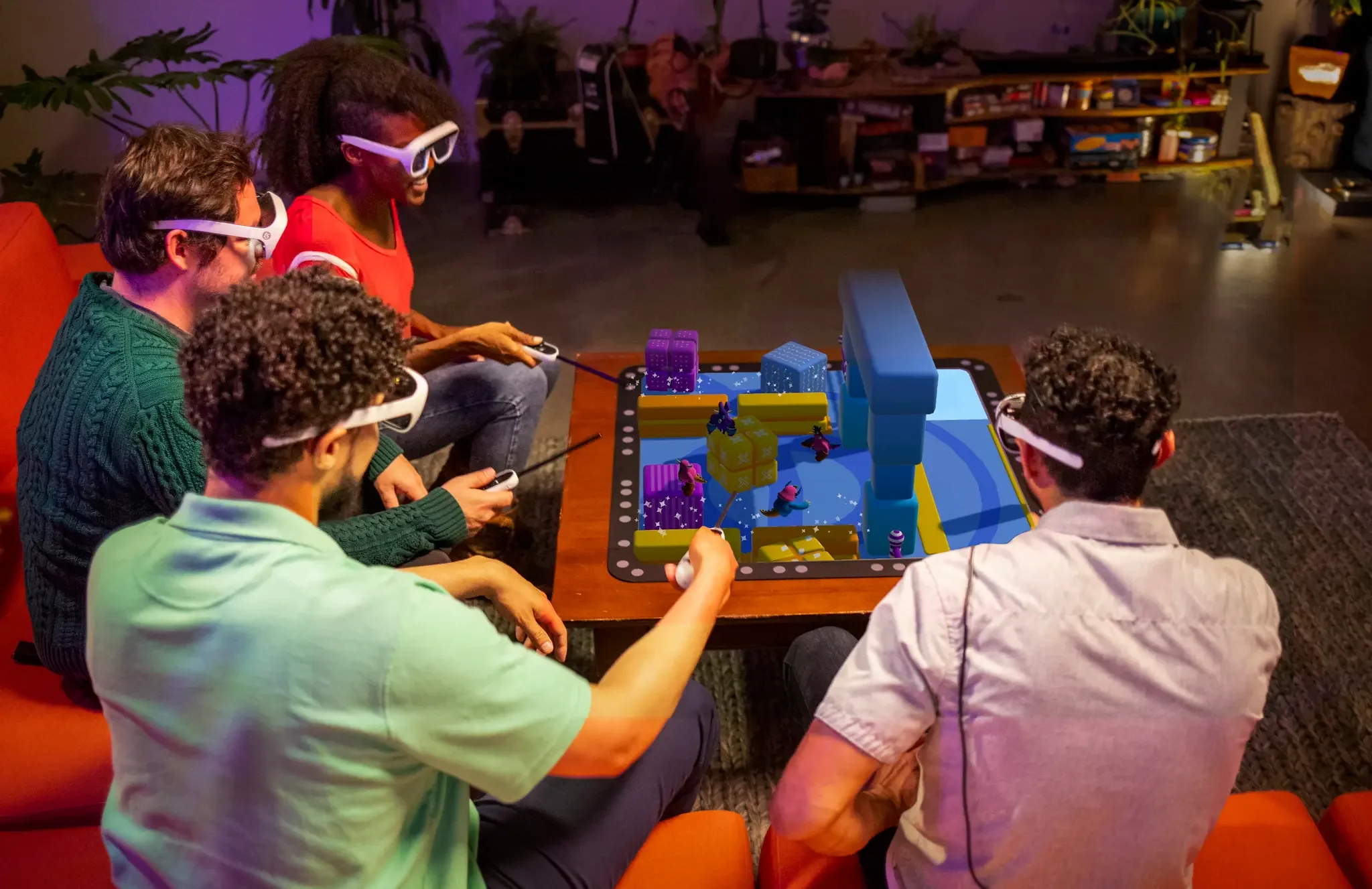Three people wearing Tilt Five AR glasses playing a tabletop AR game together in a living room, with a colorful 3D game world projected above a board placed on the coffee table