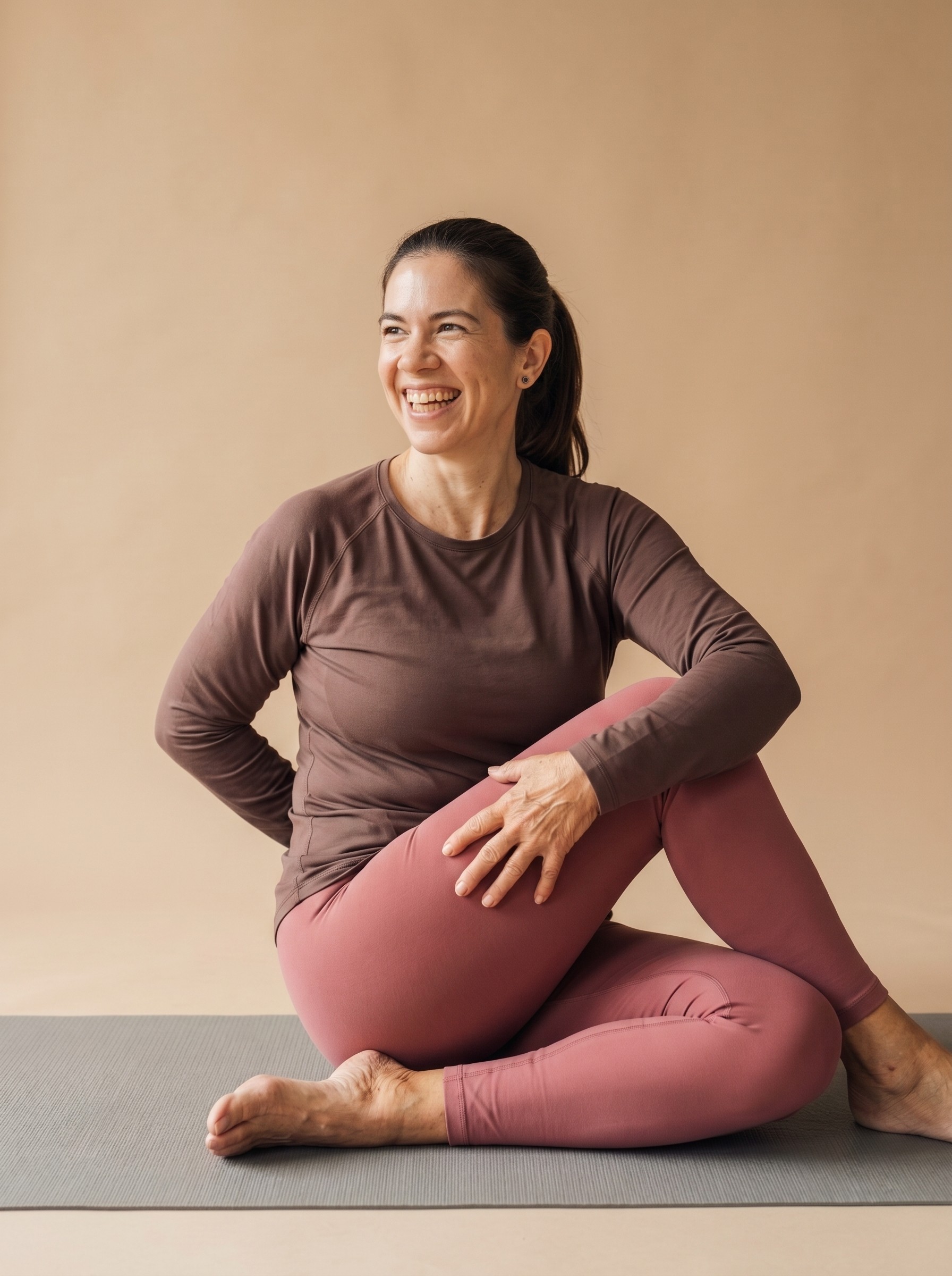 Woman in a pink sports bra and brown biker shorts smiling mid-stretch during a power vinyasa pose